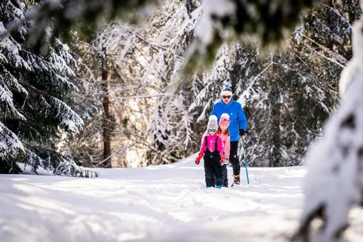 Famille marchant dans la neige en forêt dans le Haut-Jura